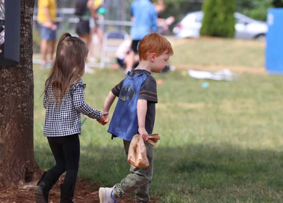 Two preschool students holding hands and walking though the field