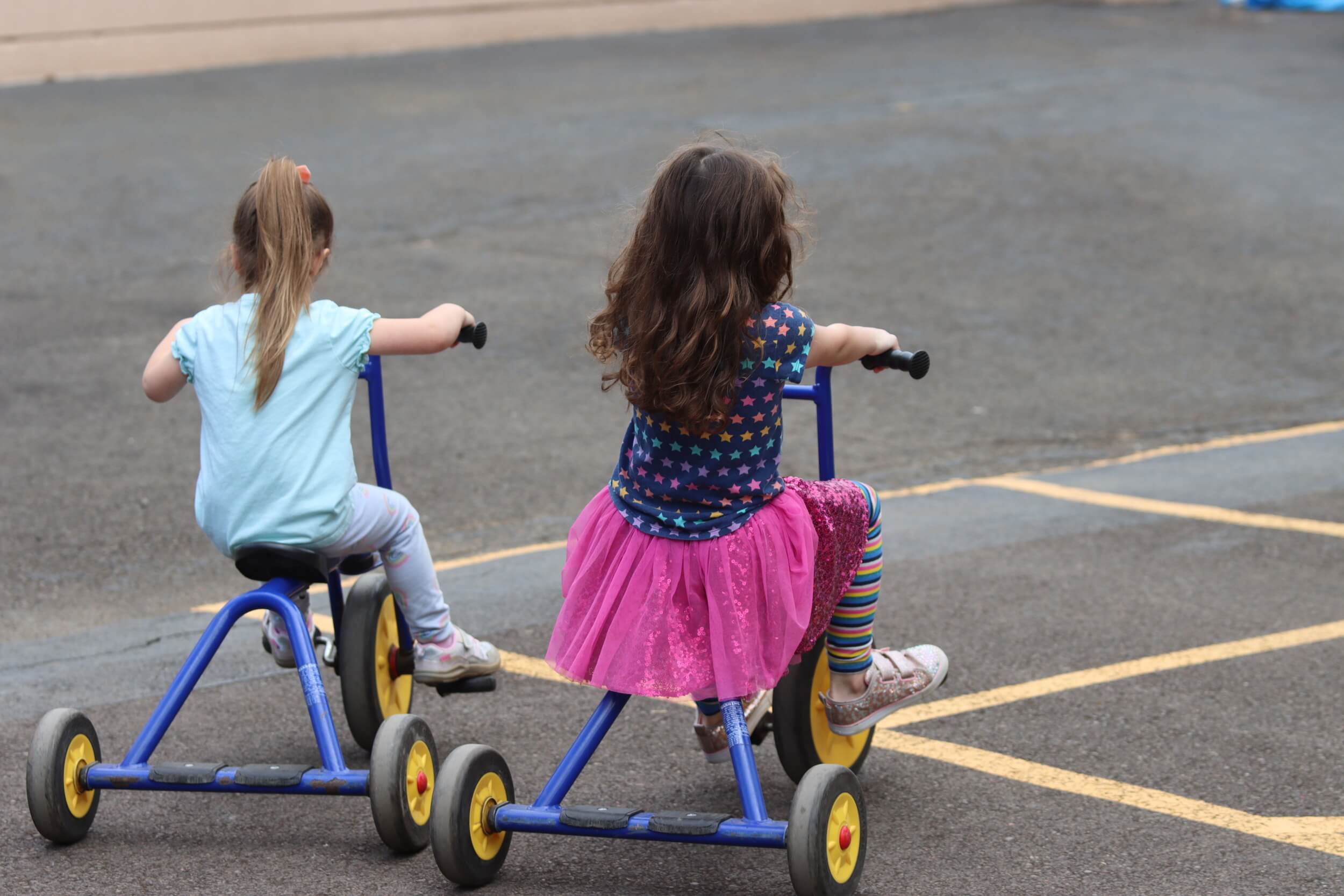 Two kindergarten students riding tricycles together at recess