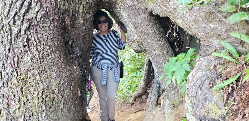 Becky smiling as she ducks on a pathway under large tree roots.
