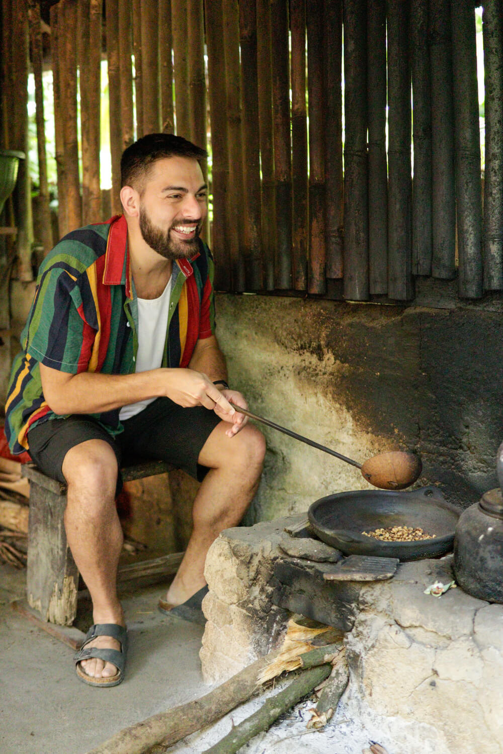 Nick sitting in a tropical hut cooking nuts over a fire.