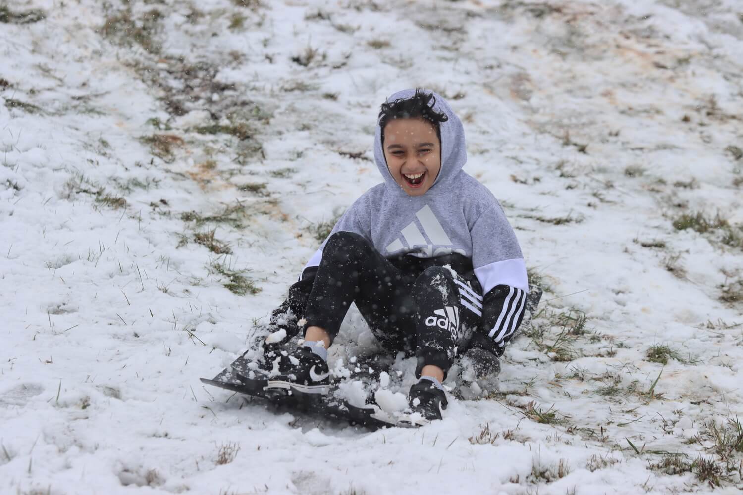 A student screaming with laughter as they sled down the snowy hill at the school.