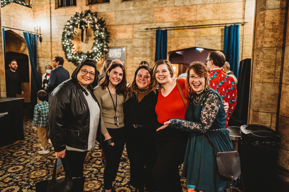 A handful of staff cheerfully posing for a photo at a holiday concert.