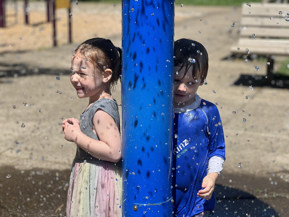 Two preschoolers soaked in water, laughing at a water spout